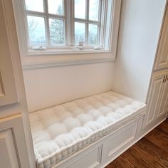 a white bench sitting under a window in a room with wooden floors and cabinets on either side