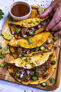 a wooden cutting board topped with tacos and sauce