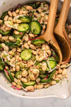 a bowl filled with beans, cucumbers and other vegetables next to a wooden spoon