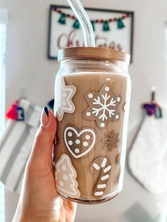 a hand holding a mason jar with christmas decorations painted on it and straw in the lid