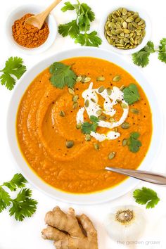 a white bowl filled with carrot soup surrounded by spices and herbs