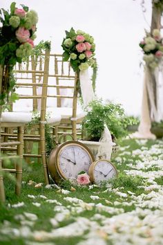 an outdoor ceremony with chairs and flowers on the grass next to a clock that is sitting in front of it