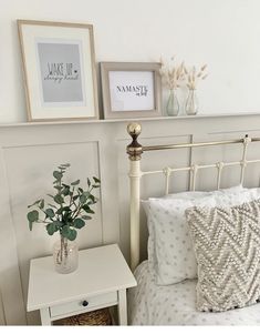 a white bed topped with pillows and a vase filled with flowers next to a night stand