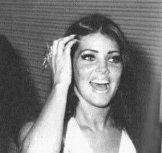 a black and white photo of a woman holding her hand up to her head while smiling