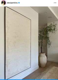 a large white vase sitting on top of a hard wood floor next to a wall