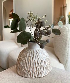 a white vase filled with flowers and greenery on a table next to a couch