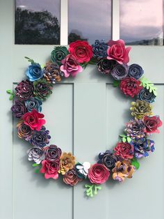 a wreath made out of paper flowers is hanging on the front door with two windows