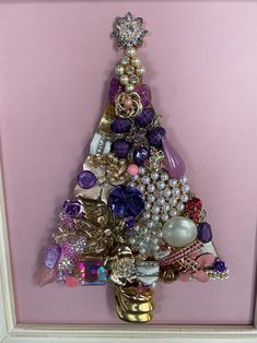 a christmas tree made out of jewelry and other items in a white frame on a pink wall