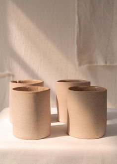 three clay cups sitting on top of a white cloth covered tablecloth, with shadows coming from the wall behind them