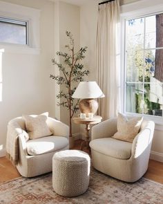 a living room with two chairs and a table in front of a large window that has a lamp on it