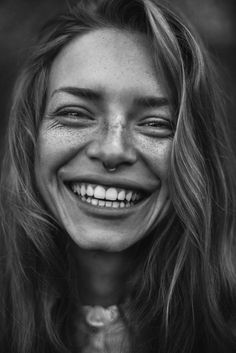 a smiling woman with long hair and freckles on her face, in black and white