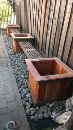 three wooden benches sitting next to each other on top of a gravel covered ground near a fence