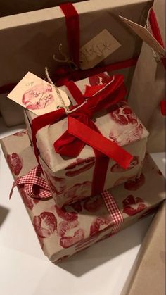 two wrapped presents with red ribbon and tags on them sitting on top of each other