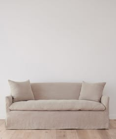 a couch sitting on top of a hard wood floor next to a white wall with two pillows