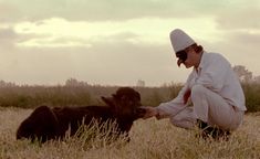 a man kneeling down next to a baby cow