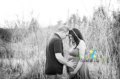 a man and woman standing in tall grass with their hands on the belly of each other