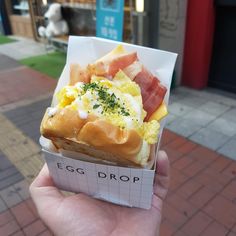 someone holding up a sandwich with eggs, ham and cheese on it in front of a store