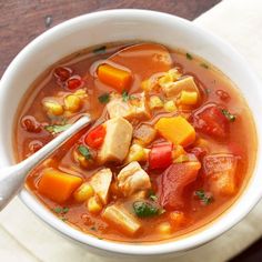 a bowl of chicken and vegetable soup with a spoon in it on a napkin next to a wooden table