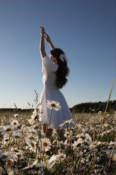 a woman in a field of daisies reaching up to the sky