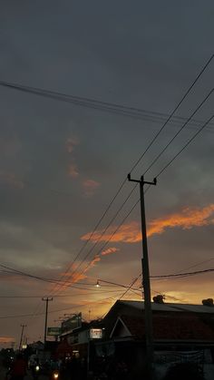 the sun is setting behind power lines and telephone poles in an urban area with cars parked on the street