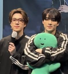 two young men standing next to each other while holding a stuffed animal in their arms