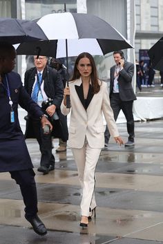 a woman holding an umbrella while walking down the street with another man in suit and tie