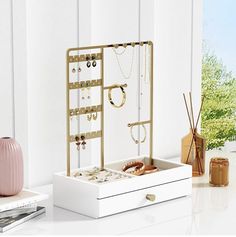 a white box with jewelry on it sitting next to a pink vase and other items