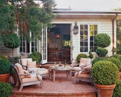 a patio with chairs, tables and potted plants in front of a house that has an open door