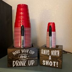 two red cups with writing on them are sitting next to each other in front of a wooden sign that says drink up