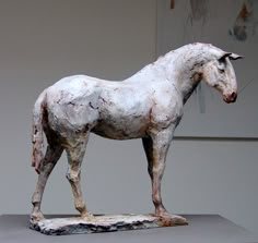 a sculpture of a white horse standing on top of a gray table next to a wall