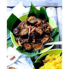 a green plate topped with meat and rice next to another bowl filled with yellow rice