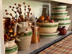 bowls and pitchers are lined up on a shelf in a kitchen with plaid tablecloth