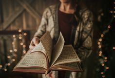 a woman is holding an open book in her hands while standing next to christmas lights