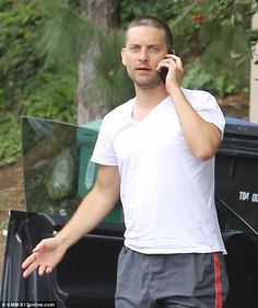 a man talking on a cell phone while standing in front of a garbage can with his hands out