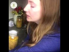 a woman is standing in front of jars with food on the counter and flowers behind her