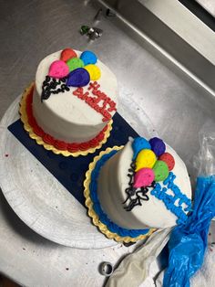 two decorated birthday cakes sitting on top of a metal counter next to a blue bag