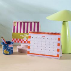 a desk with a calendar, pen holder and lamp on it next to other items