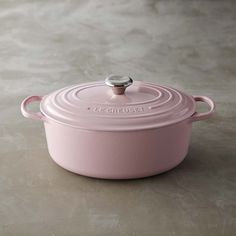 a pink casserole dish with a lid on the counter top, sitting on a table