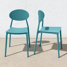 two blue chairs sitting next to each other in front of a white wall and cement floor