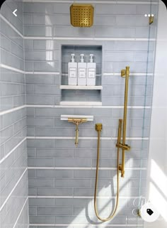 a white and gold tiled bathroom with shower head, soap dispenser, and shelves