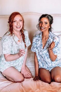 two women sitting on top of a bed next to each other wearing matching shirts and shorts