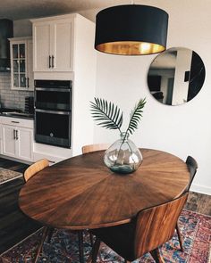 a dining room table that has a vase with a plant in it and two mirrors on the wall