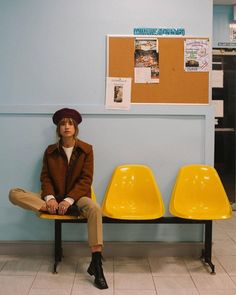 a woman sitting on top of a yellow chair in front of a bulletin board wall