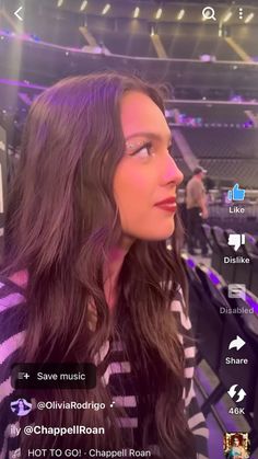 a woman with long dark hair is on her cell phone at a concert and looks off into the distance