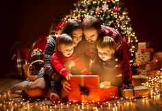 a family opening a christmas present in front of a christmas tree with lights on it