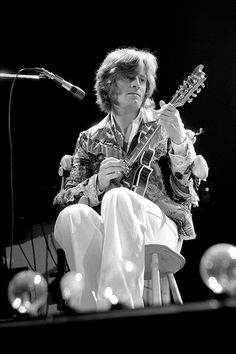 a man sitting on top of a chair playing a guitar in front of a microphone