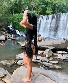 a woman standing on top of a rock next to a river with waterfall in the background