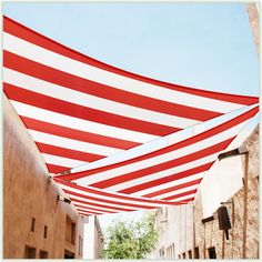 a large red and white striped awning in an alleyway with buildings behind it