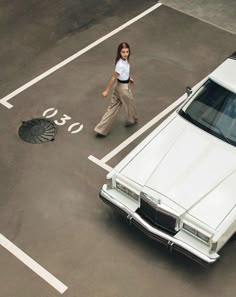 a woman walking past a white car in a parking lot