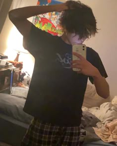 a young boy is taking a selfie in his bedroom while wearing plaid shorts and a black t - shirt